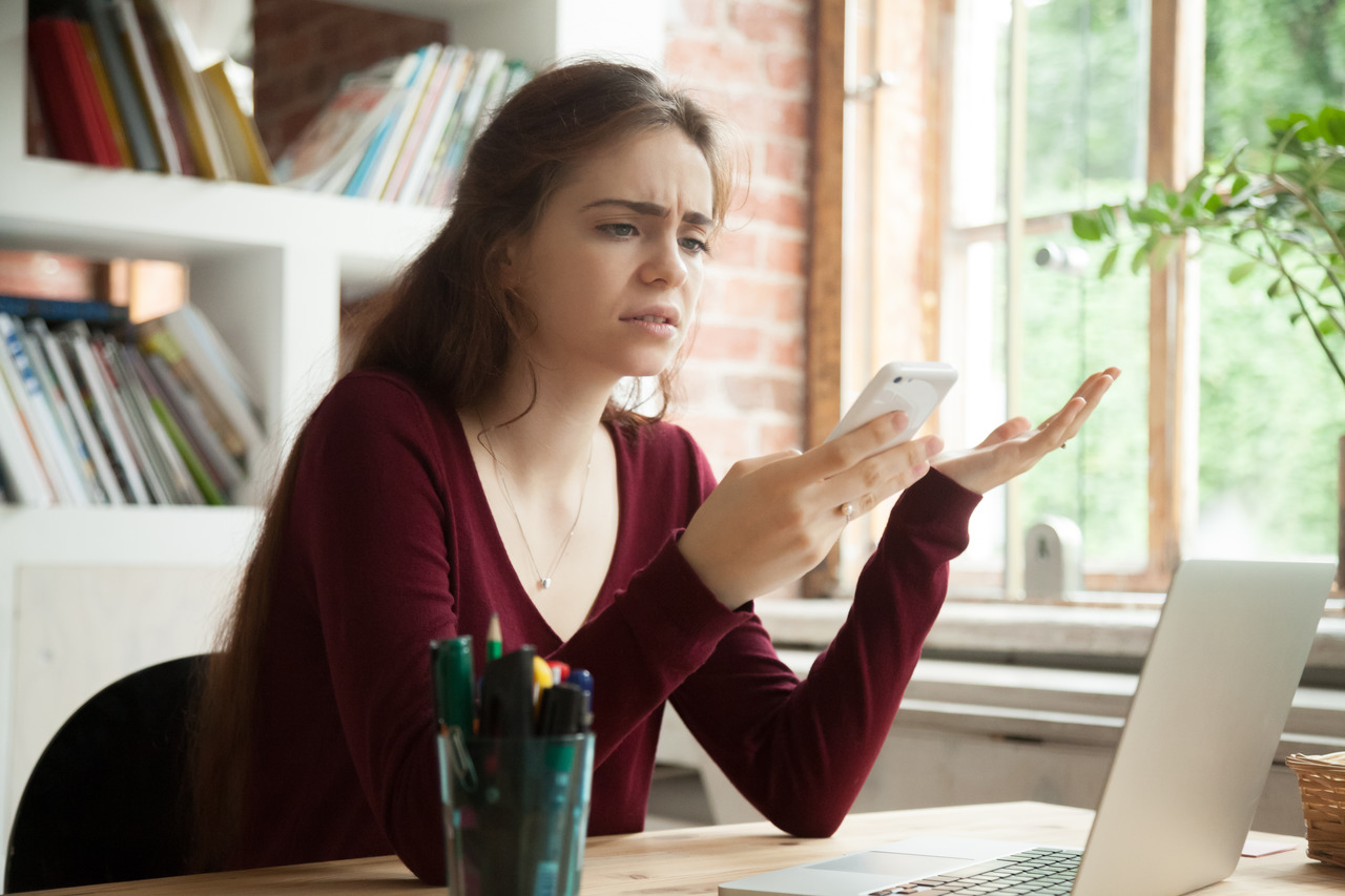 Mulher olhando para a tela do celular com uma feição de irritação. Saber como aumentar a velocidade da internet pode deixar o seu dia muito mais produtivo.