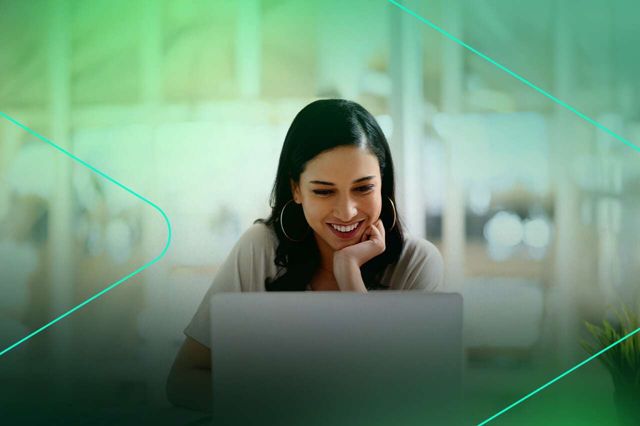 Mulher sorrindo enquanto usa laptop em ambiente de escritório.